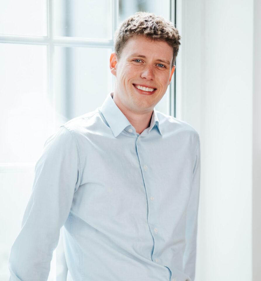 Porträtfoto von Lenno für die Teamseite von Heykes&Karstens, stehend und im Hintergrund ein Fenster