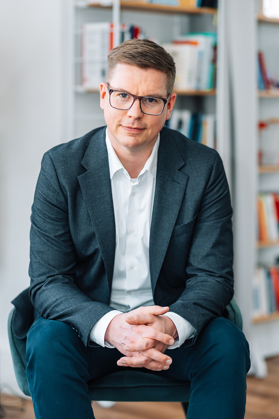 Porträtfoto von Arne Heykes für die Teamseite von Heykes&Karstens, sitzend vor Bücherregal