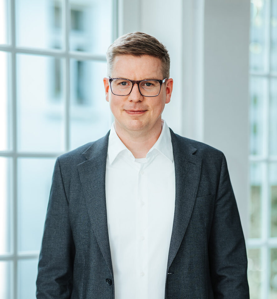 Porträtfoto von Arne Heykes für die Teamseite von Heykes&Karstens, stehend und im Hintergrund ein Fenster