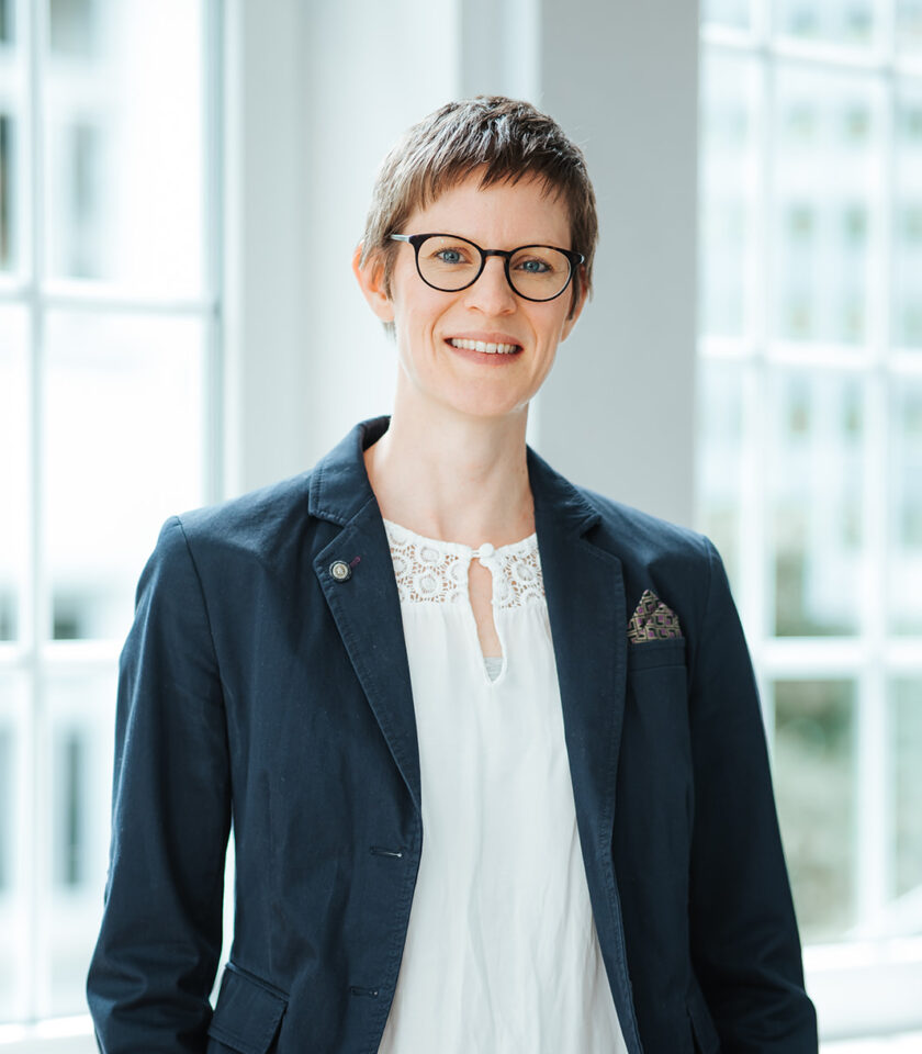 Porträtfoto von Dr. Friederike Teetzen für die Teamseite von Heykes&Karstens, stehend und im Hintergrund ein Fenster