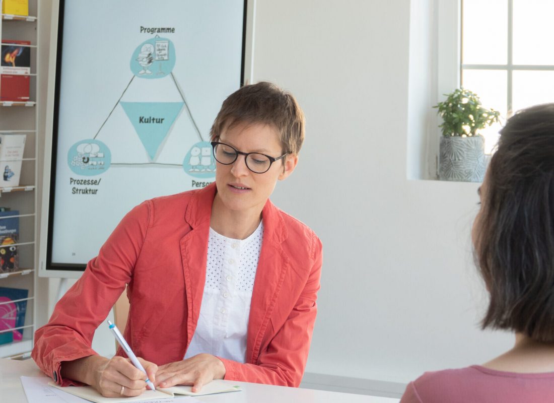 Frau Dr. Teetzen, die an einem Tisch etwas schreibt und ihr gegenüber sitzt eine Frau