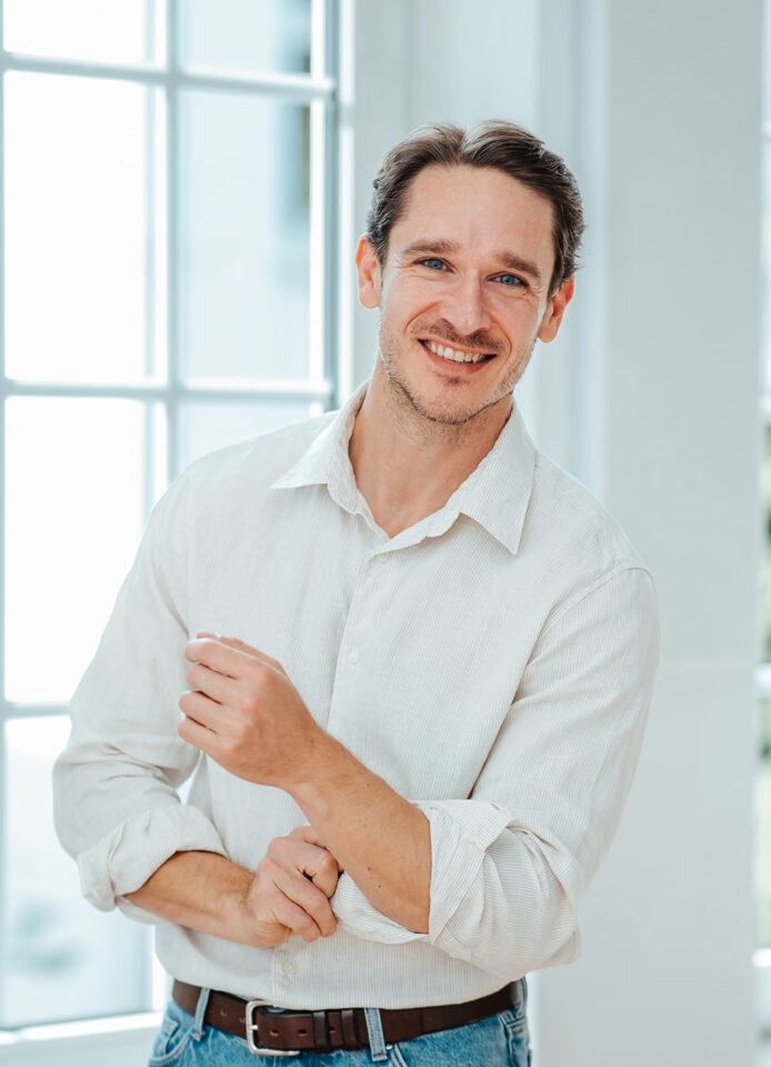 Porträtfoto von Philipp Volotas für die Teamseite von Heykes & Karstens, stehend und im Hintergrund ein Fenster